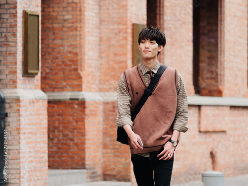 Portrait of a handsome Chinese young man with Korean style clothes walking on street in hurry in sunny day with Shanghai Nanjing road background, male fashion, cool Asian young man lifestyle. photo