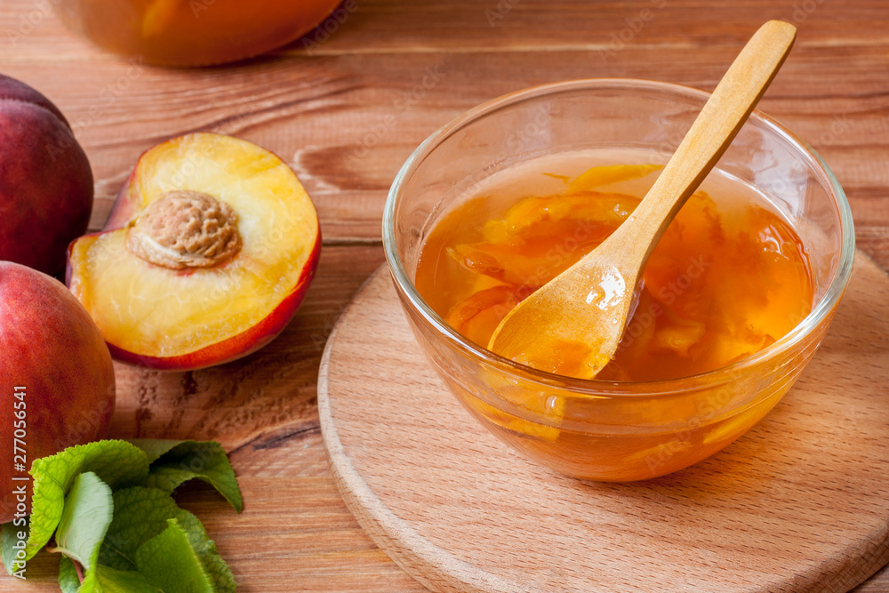 Piala with a spoon in homemade peach jam on a wooden round stand on the table in the morning sun. The concept of homemade conservation. Close up Piala with a spoon in homemade peach jam on a wooden round stand on the table in the morning sun. The concept of homemade conservation. Close up