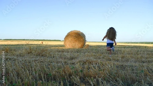 Little girl running to the stacks in the field. Slow motion.