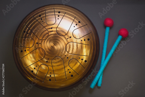 Golden hang drum with blue and red drumsticks on a black background, top view