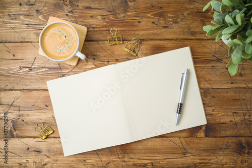 School notebook with coffee cup and plant on wooden table. Top view from above