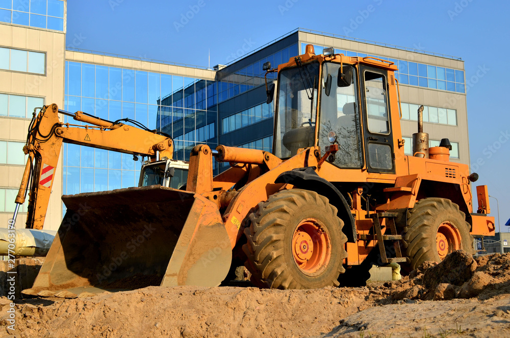 Wheel loader bulldozer with a bucket on a street in the city during the construction of the road.