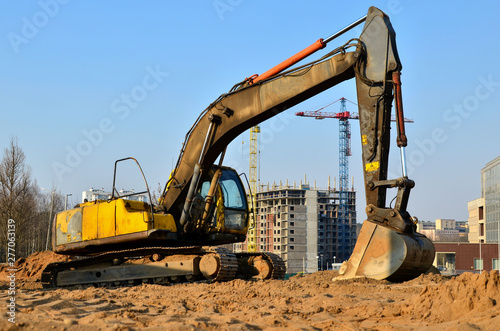 Yellow excavator at a construction site during earthworks and laying of underground pipes and communications in the city