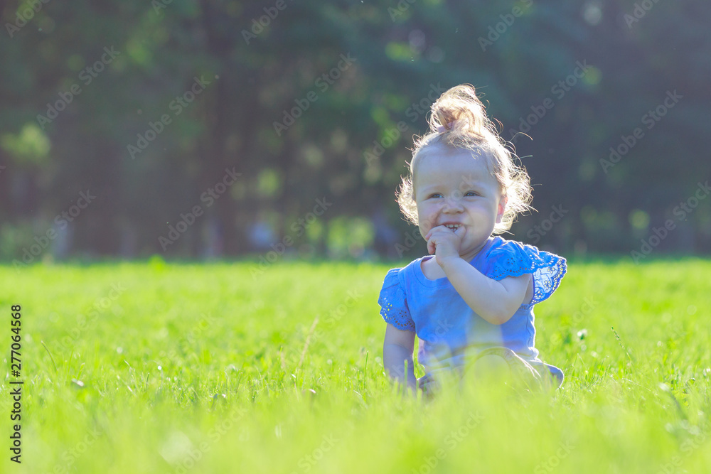 Cute little girl sits on the green grass, outdoors, summer time, blurred background Cute little girl sits on the green grass, outdoors, summer time, blurred background