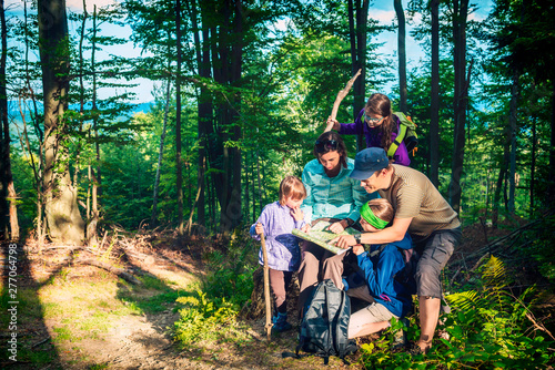 Happy family - father, mother and three daughters - on a mountain trip in the forest looking at the map