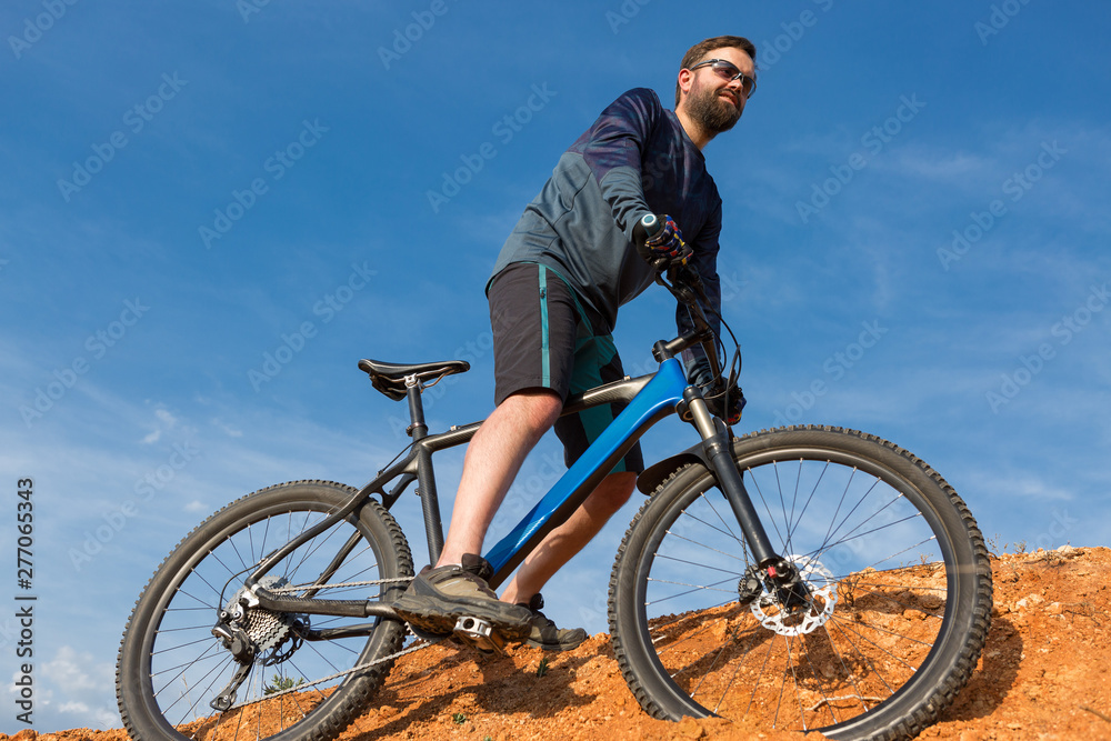 Cyclist in shorts and jersey on a modern carbon hardtail bike with an air suspension fork rides off-road on the orange-red hills at sunset evening in summer	