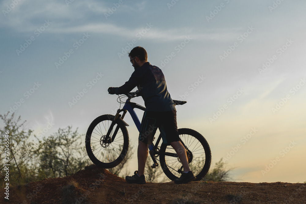 Cyclist in shorts and jersey on a modern carbon hardtail bike with an air suspension fork rides off-road on the orange-red hills at sunset evening in summer	