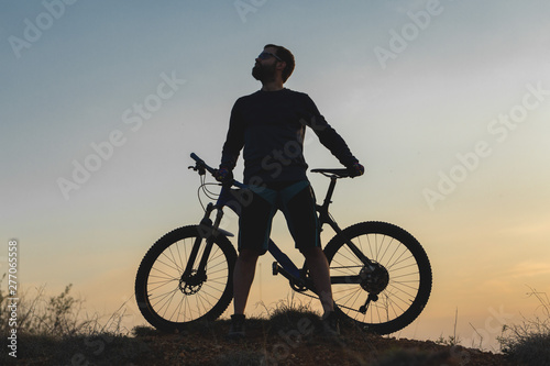 Cyclist in shorts and jersey on a modern carbon hardtail bike with an air suspension fork rides off-road on the orange-red hills at sunset evening in summer 