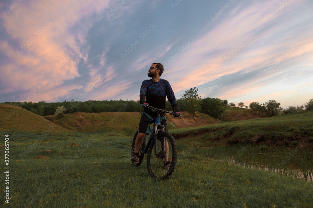 Cyclist in shorts and jersey on a modern carbon hardtail bike with an air suspension fork rides off-road on the orange-red hills at sunset evening in summer Cyclist in shorts and jersey on a modern carbon hardtail bike with an air suspension fork rides off-road on the orange-red hills at sunset evening in summer