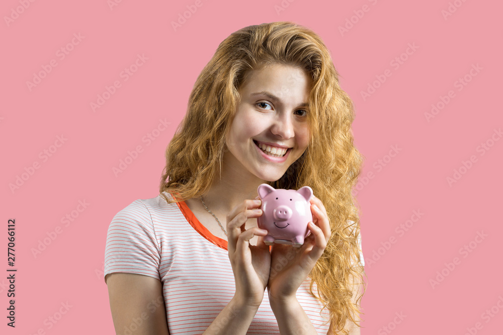 Young red-haired curly girl holding piggy bank and rejoices gesturing. The concept of reliability of cash investments and insurance.