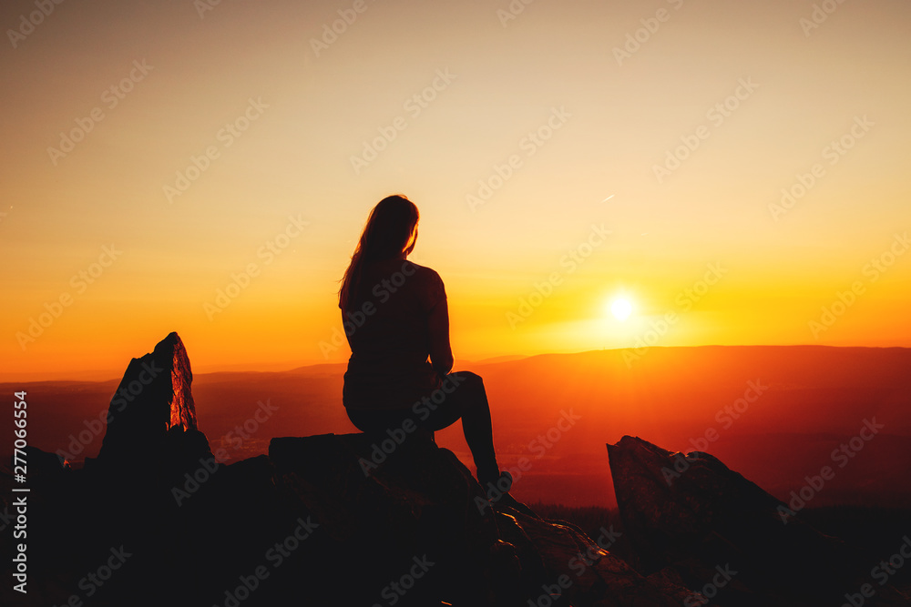 A girl silhouette sitting chilling on the mountain top and watching sunset on a warm summer day. Torfhaus, National Park Harz in Germany