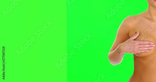 Half view of nude woman covering her breasts with hand on green screen background.