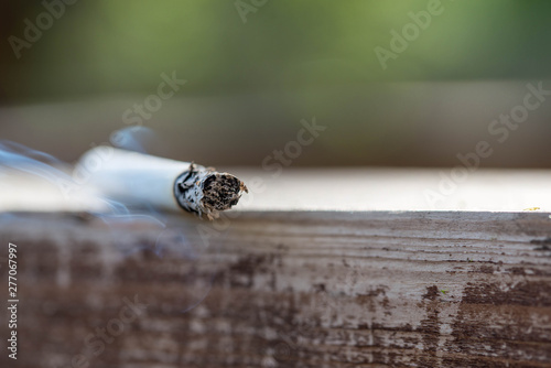 Burning cigarette on wooden surface close up macro shot, conceptual image of human negligence.