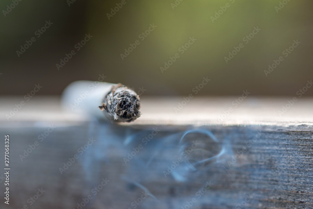 Burning cigarette on wooden surface close up macro shot, conceptual image of human negligence. Burning cigarette on wooden surface close up macro shot, conceptual image of human negligence.