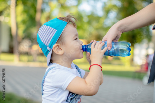 Tablou pe pânză a little boy in a cap with a smile drinking water from a bottle in the Park
