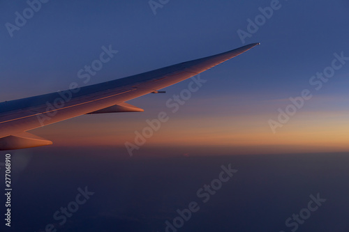 wing of airplain flying over the clouds with blue sky before sunset
