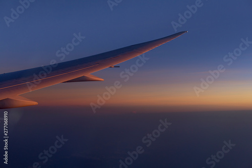 wing of airplain flying over the clouds with blue sky before sunset photo
