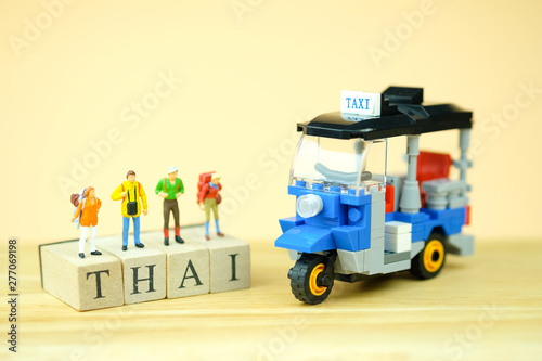 Miniature tourist standing on wooden word is THAI near Tuk tuk