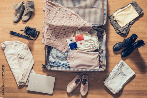 Woman's clothes, laptop, camera, russian passport and flag of Panama lying on the parquet floor near and in the open suitcase. Travel concept