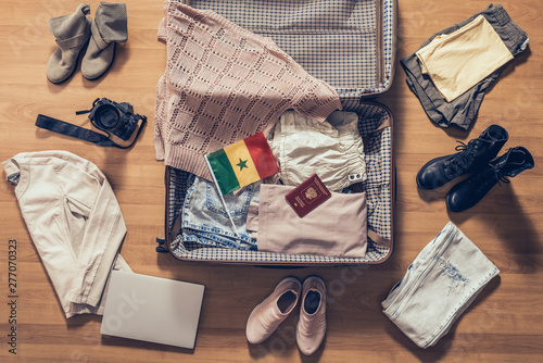 Woman's clothes, laptop, camera, russian passport and flag of Senegal lying on the parquet floor near and in the open suitcase. Travel concept