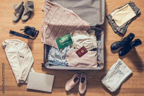 Woman's clothes, laptop, camera, russian passport and flag of Saudi Arabia lying on the parquet floor near and in the open suitcase. Travel concept