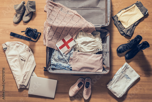 Woman's clothes, laptop, camera and flag of England lying on the parquet floor near and in the open suitcase. Travel concept