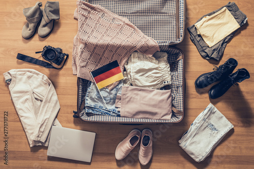 Woman's clothes, laptop, camera and flag of Germany lying on the parquet floor near and in the open suitcase. Travel concept