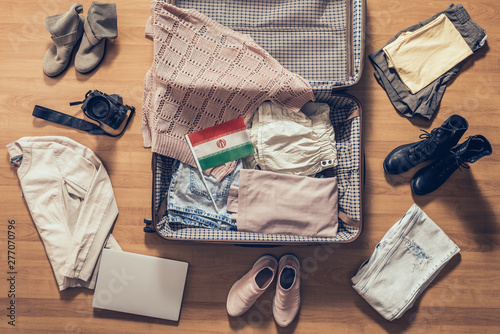 Woman's clothes, laptop, camera and flag of iran lying on the parquet floor near and in the open suitcase. Travel concept
