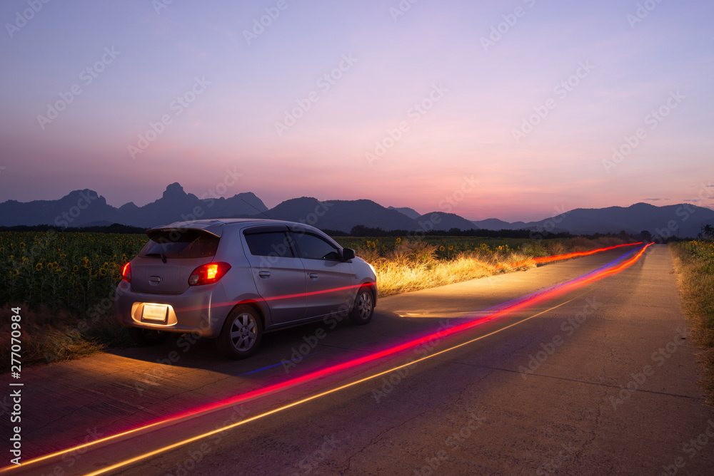 Travel car is parking at the road country side with landscape view beautiful sunset and light trails.