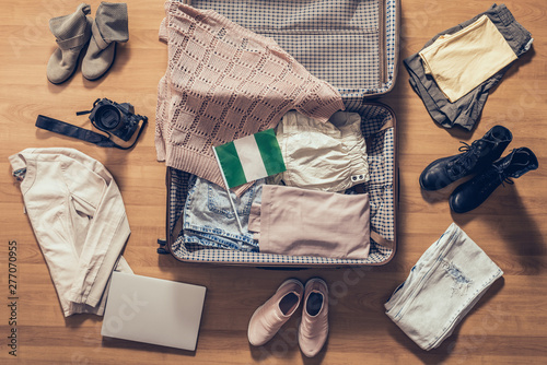 Woman's clothes, laptop, camera and flag of Nigeria lying on the parquet floor near and in the open suitcase. Travel concept