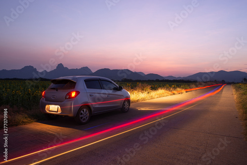 Travel car is parking at the road country side with landscape view beautiful sunset and light trails.