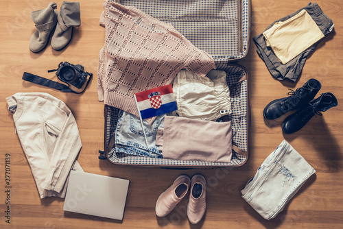 Woman's clothes, laptop, camera and flag of Croatia lying on the parquet floor near and in the open suitcase. Travel concept