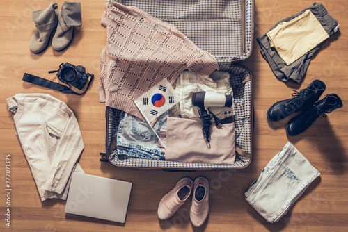 Woman's clothes, laptop, camera and flag of South Korea lying on the parquet floor near and in the open suitcase. Travel concept