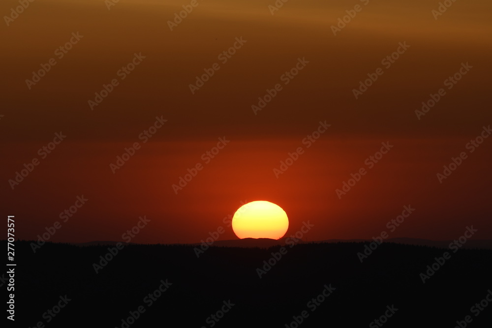 Giant sun with mountain sunset and silhouettes and warm orange color tones. Torfhaus, National Park Harz in Germany Giant sun with mountain sunset and silhouettes and warm orange color tones. Torfhaus, National Park Harz in Germany