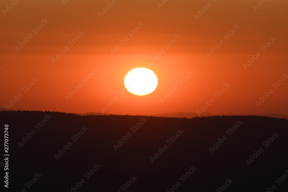Giant sun with mountain sunset and silhouettes and warm orange color tones. Torfhaus, National Park Harz in Germany Giant sun with mountain sunset and silhouettes and warm orange color tones. Torfhaus, National Park Harz in Germany