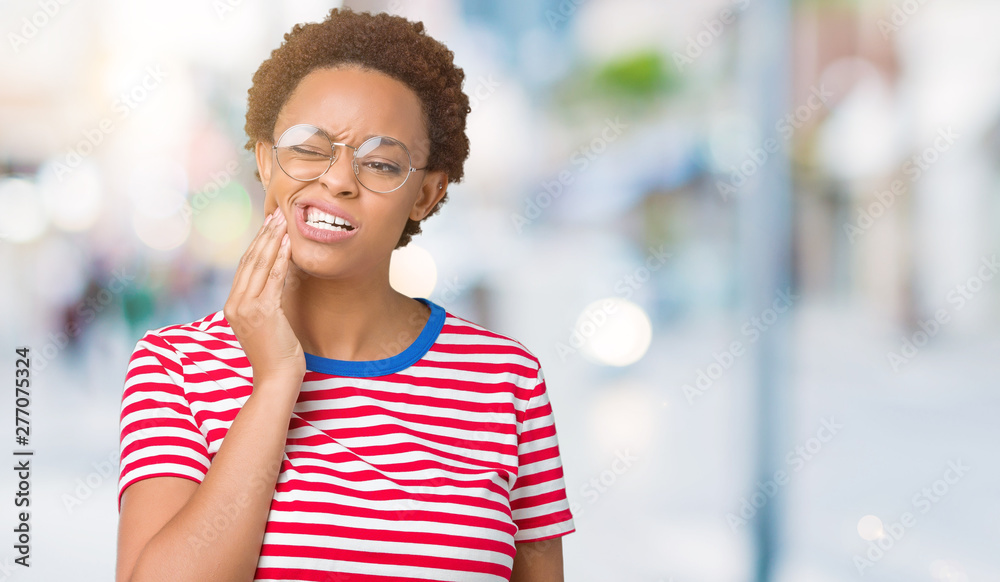 Beautiful young african american woman wearing glasses over isolated background touching mouth with hand with painful expression because of toothache or dental illness on teeth. Dentist concept.