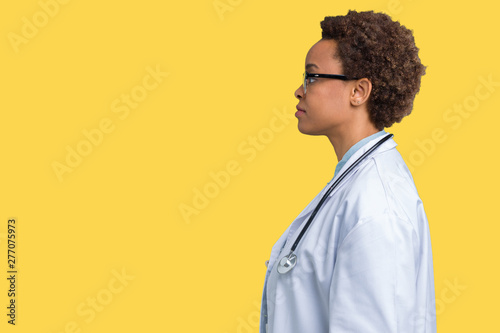 Young african american doctor woman wearing medical coat over isolated background looking to side, relax profile pose with natural face with confident smile.