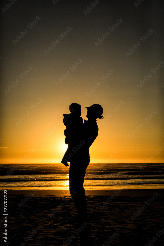 silhouette of woman holding child on the beach at sunset