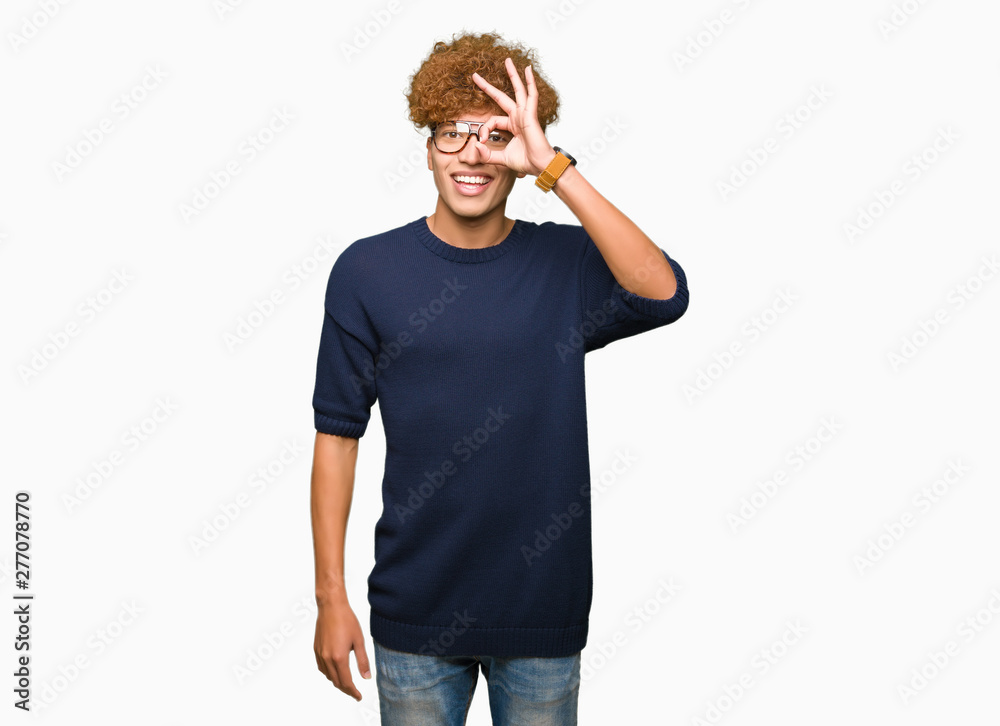 Fototapeta premium Young handsome man with afro wearing glasses doing ok gesture with hand smiling, eye looking through fingers with happy face.