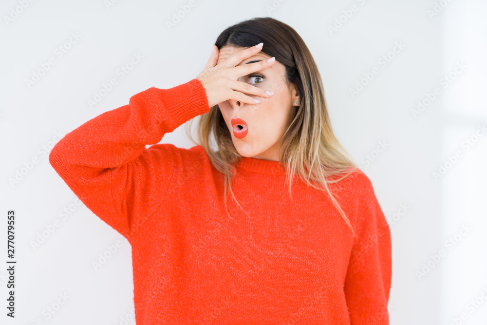 Young woman wearing casual red sweater over isolated background peeking in shock covering face and eyes with hand, looking through fingers with embarrassed expression. Young woman wearing casual red sweater over isolated background peeking in shock covering face and eyes with hand, looking through fingers with embarrassed expression.
