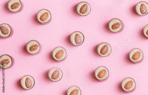 Round chocolates with pistachio cream and salted almonds on pink background. Flat lay