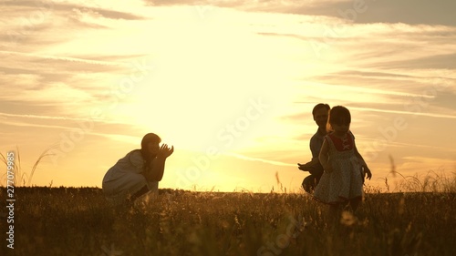 Mom and Dad playing with their daughter in park at sunset. kid takes the first steps. Happy family playing with the child in rays of sun. baby goes from dad to mom and laughs. Slow motion.