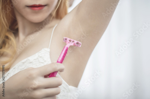 Young woman shaving her armpit epilation hair removal with pink shaver.
