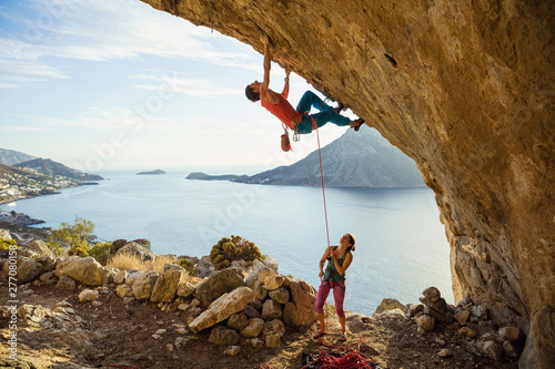 Young man starts climbing in cave, his female partner belaying him photo