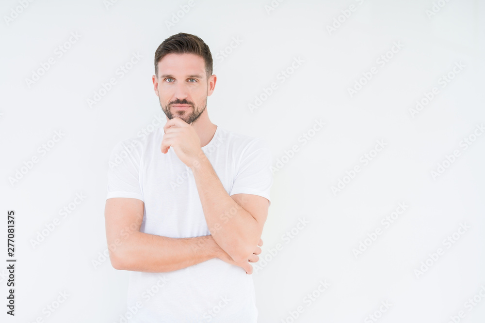 Young handsome man wearing casual white t-shirt over isolated background looking confident at the camera with smile with crossed arms and hand raised on chin. Thinking positive.