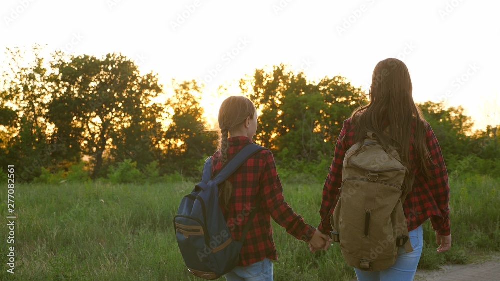 tourist girls on country road. Hiker Girl. teen girls travel and hold hands. children travelers. girls with backpacks are on country road in sun. concept of sports tourism and travel.
