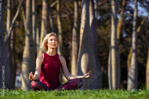 Beautiful people Fitness woman with short blonde hair doing yoga, concentrate and smile in a park of bottle trees, sitting on the grass. Sport and Healthy Lifestyle Concept © Serega777