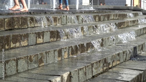 Barefoot legs play with fountain water jets. People in town play with water in the fountains, happy and carefree, concept of freedom and happiness in childhood, starting summer and tourist cities.