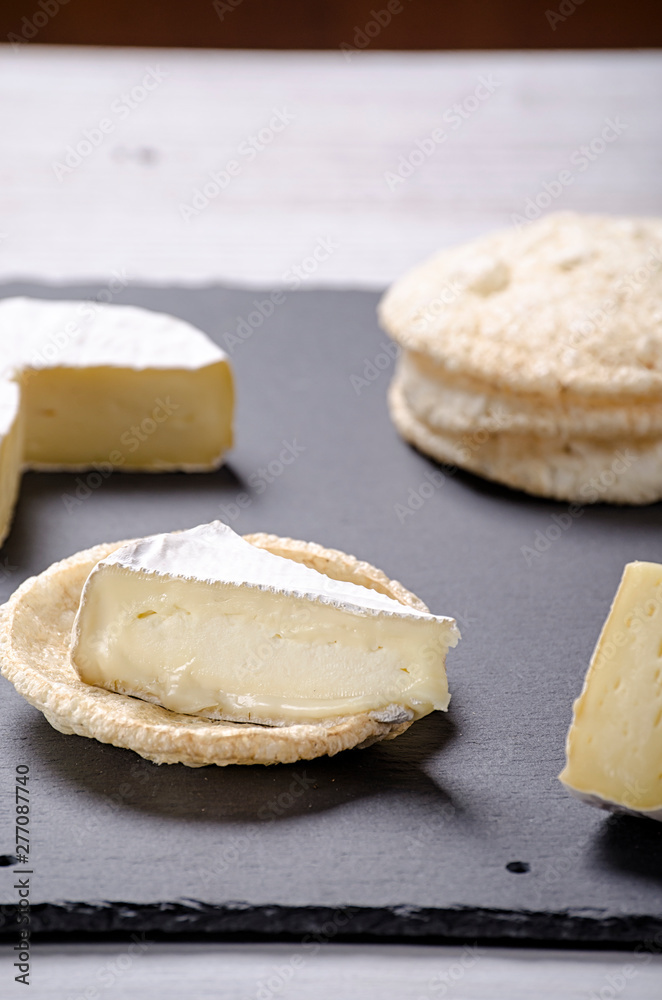 brie de famille cheese and small round loaves lie on a slate Board on a white wooden background, round cheese, sliced cheese on bread