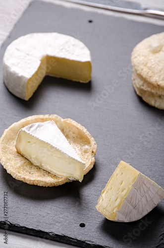 brie de famille cheese and small round loaves lie on a slate Board on a white wooden background, round cheese, sliced cheese on bread